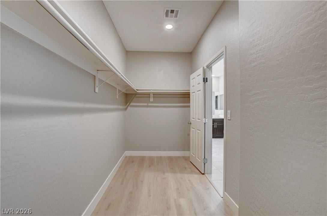 Ample built-in shelving and smooth wood-style flooring line this master walk-in closet.