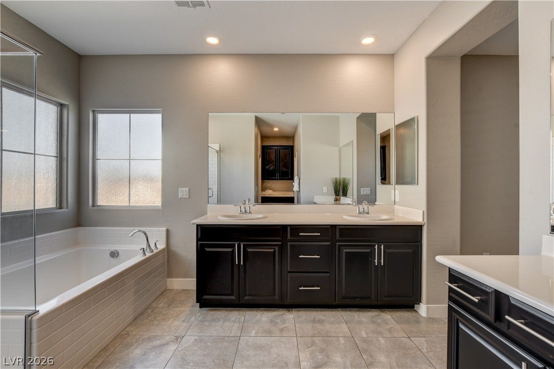A spacious master bathroom features a double vanity and a built-in soaking tub under tile flooring.