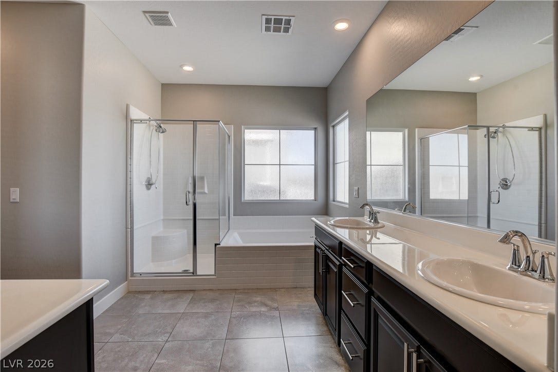 A spacious bathroom features a dual-sink vanity, a tiled floor, and a separate glass shower.