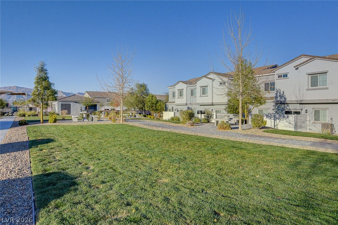 An open green belt area with paved walkways is situated adjacent to residential townhomes.