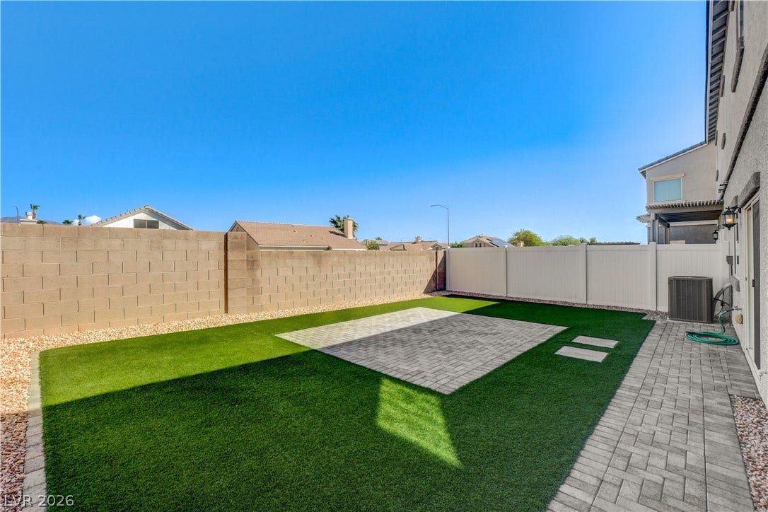 An enclosed backyard features a clean paved patio alongside vibrant low-maintenance synthetic turf.