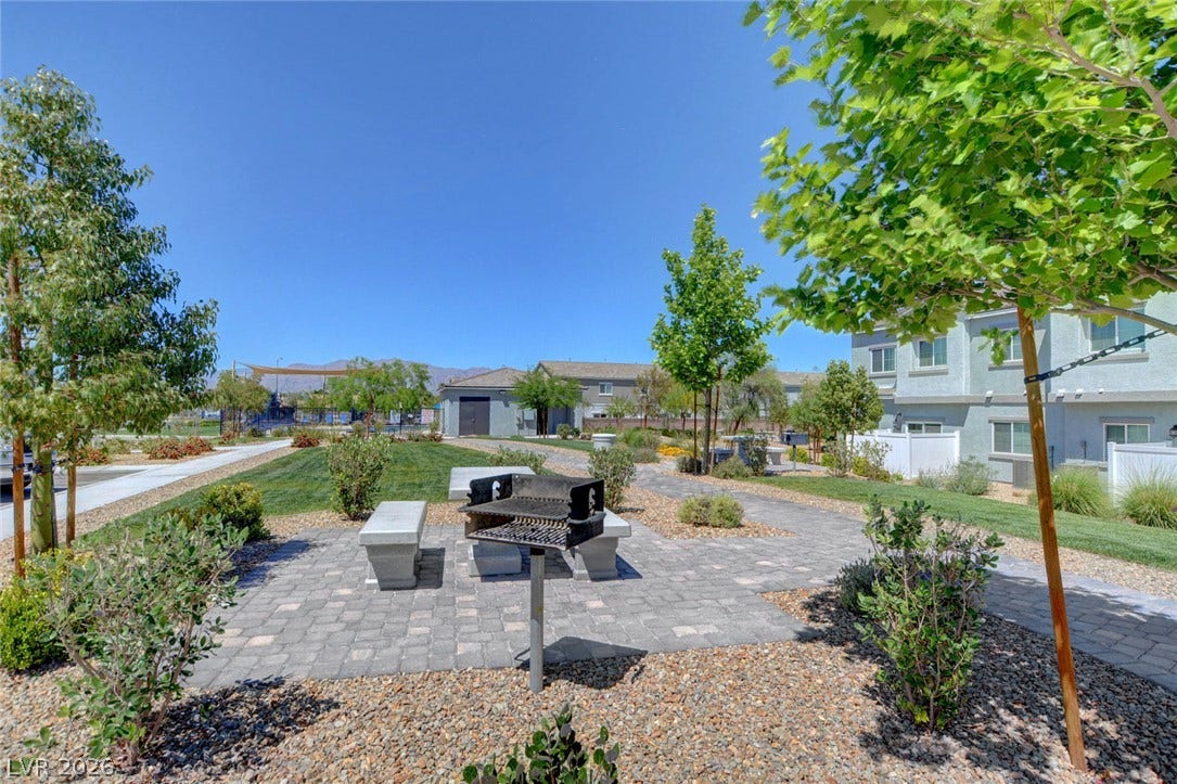 An inviting outdoor common area features a built-in barbecue grill alongside paved walkways and green lawns.
