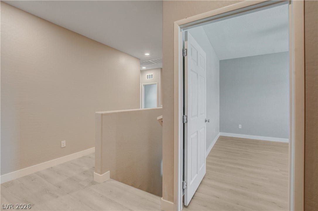 Smooth wood flooring flows from the upper landing into a bright, neutral bedroom.