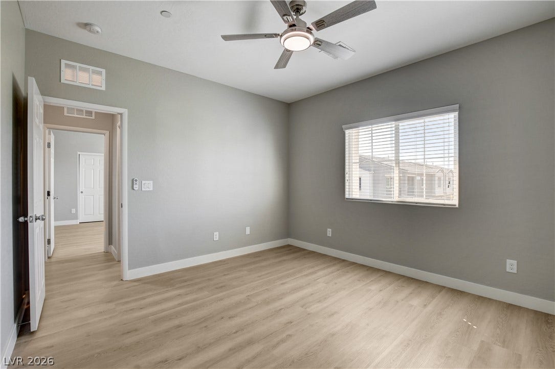 Smooth wood-look flooring and a wide window with plantation shutters define this inviting bedroom space.