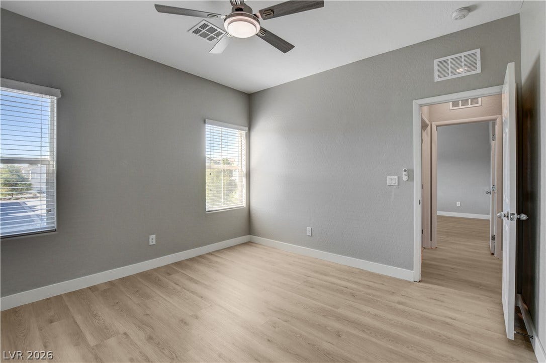 Smooth wood flooring and tall windows create a serene, well-proportioned secondary bedroom space.