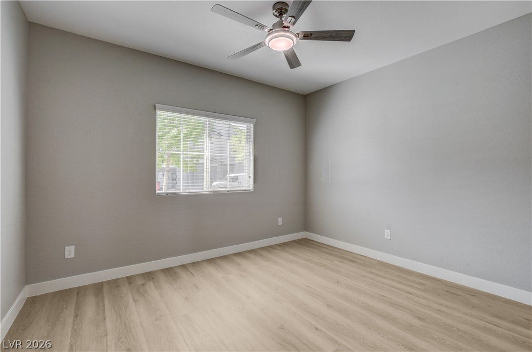 Smooth wood-style flooring anchors this versatile space under high ceilings and a central window.