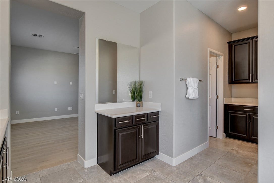 Recessed lighting illuminates the elegant vanity area finished with sleek stone counters and tile flooring.