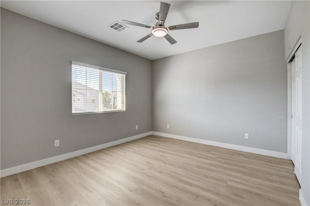 Smooth wood-look flooring and a wide window with blinds elevate this versatile bedroom.
