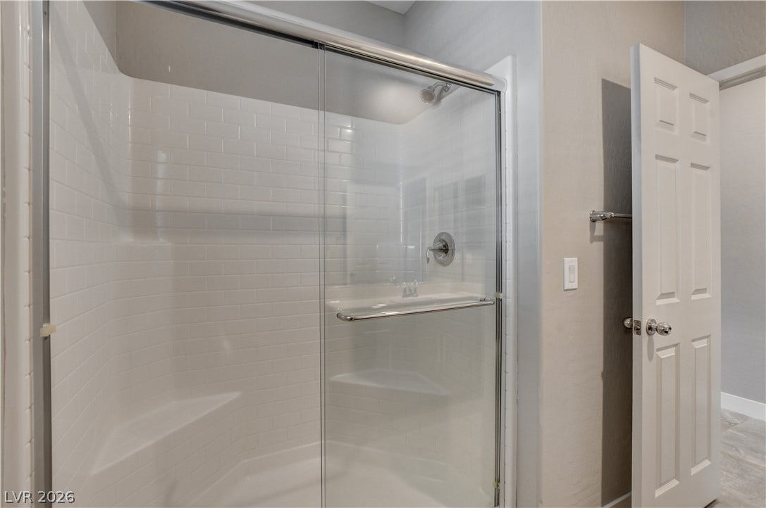 White subway tile lines the spacious walk-in shower featuring glass sliding doors.