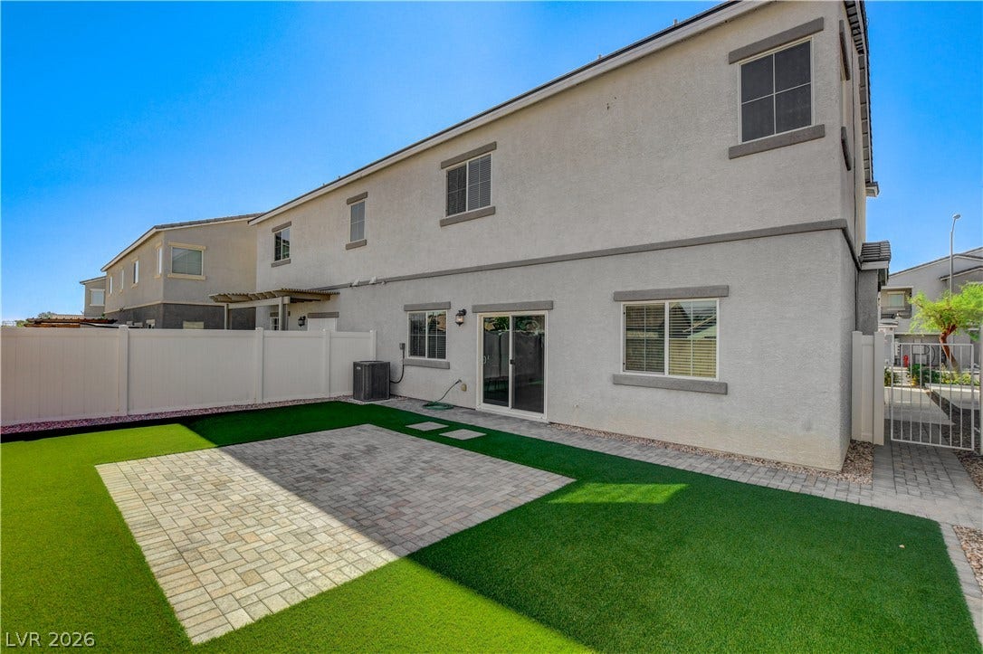 An inviting backyard features a pristine paver patio surrounded by lush artificial turf.