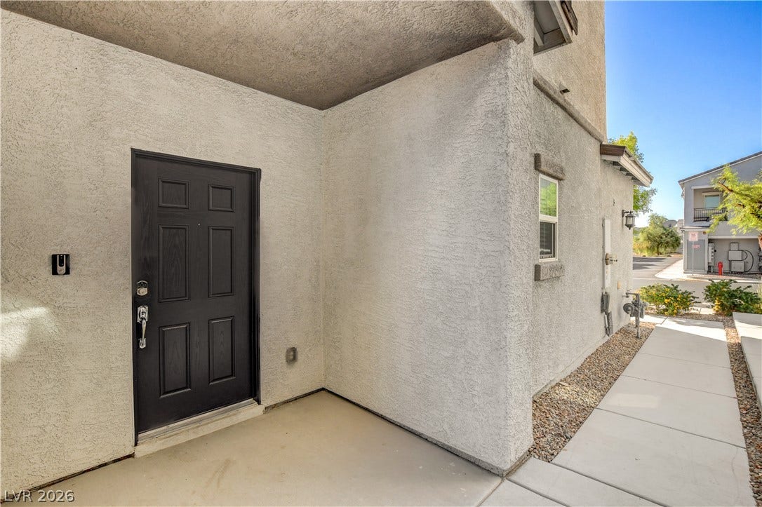 A concrete walkway leads past stucco walls to a covered entrance with a classic panel door.