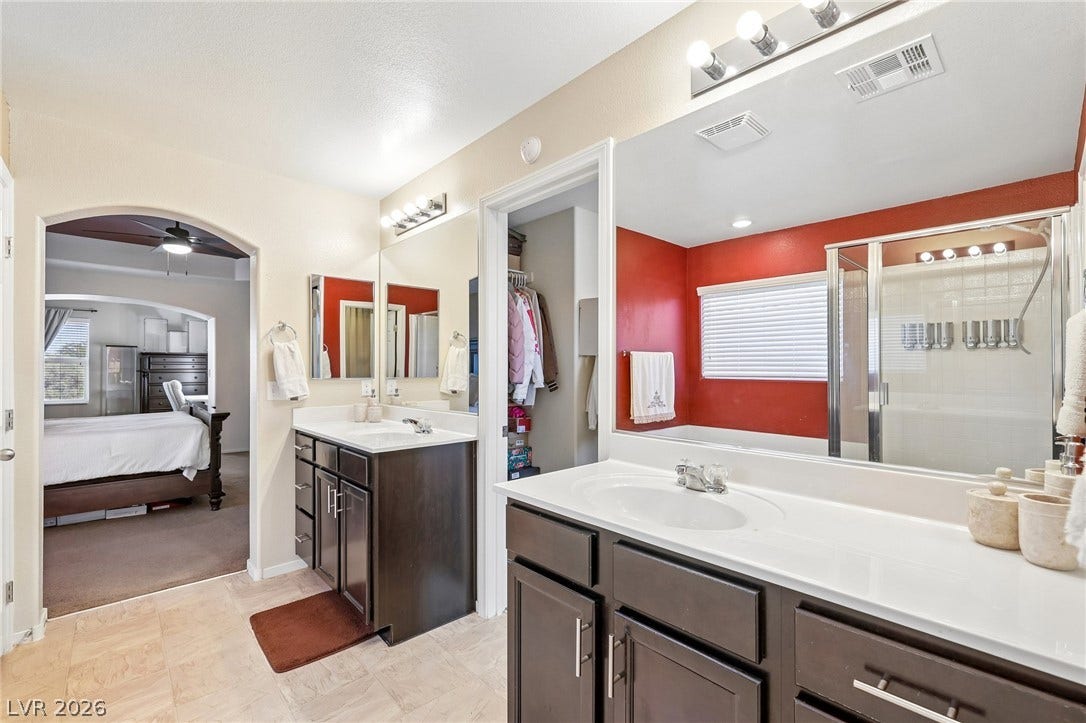 4024 Solar System Street, North Las Vegas, NV 89032 A spacious bathroom features dual dark wood vanities and tiled flooring leading to a bedroom.
