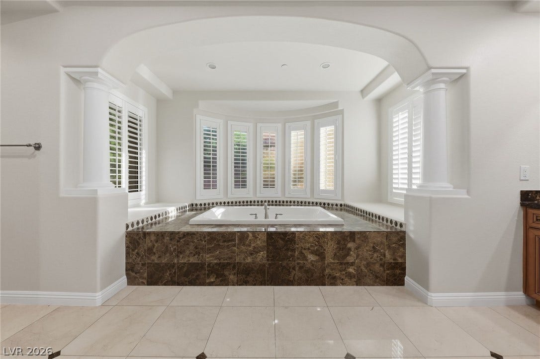 1357 Enchanted River Drive, Henderson, NV 89012 An arched alcove frames a deep soaking tub clad in polished stone tile.