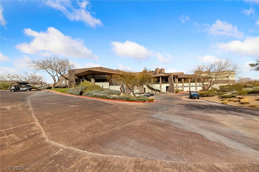 1357 Enchanted River Drive, Henderson, NV 89012 A textured concrete driveway sweeps toward a multi-level stone facade set against blue skies.
