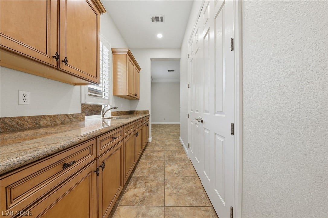 1357 Enchanted River Drive, Henderson, NV 89012 Polished stone countertops and classic cabinetry line this functional hallway utility space.