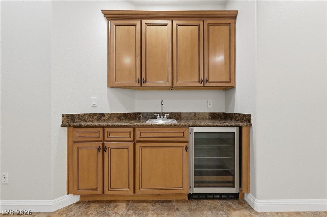1357 Enchanted River Drive, Henderson, NV 89012 A wet bar features custom wood cabinetry alongside a built-in beverage cooler and stone counters.