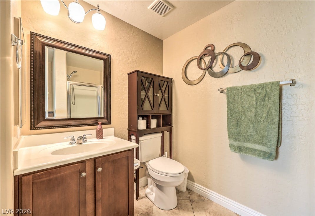 6868 Sky Pointe Drive, #1132, Las Vegas, NV 89131 Warm neutral walls complement a wood vanity and neutral tile flooring in this bathroom.