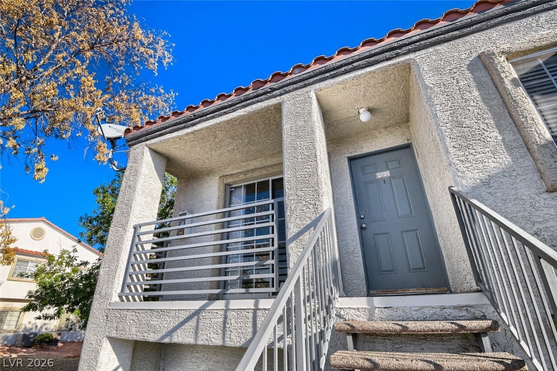 Concrete steps lead up to a covered entryway featuring Spanish tile roof accents.