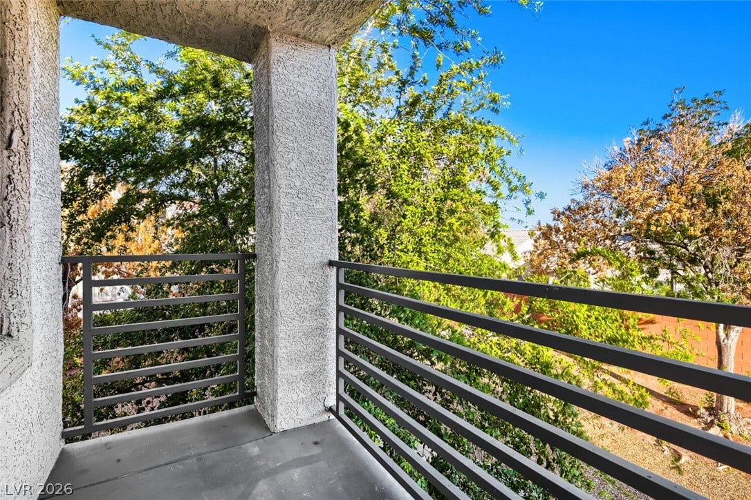 Mature trees frame the view from a private balcony bordered by sturdy metal railings.