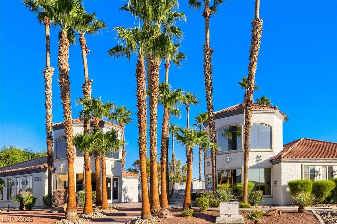 Towering palm trees frame the Mediterranean-style stucco exterior under a bright desert sky.