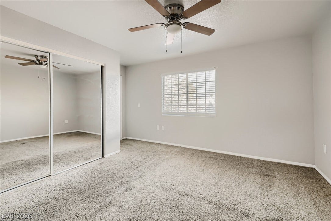 Plush carpeting anchors this clean bedroom featuring mirrored closet doors and a central window.