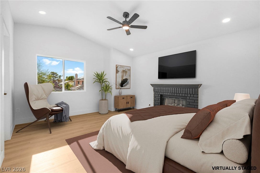 A brick fireplace anchors this bedroom space featuring vaulted ceilings and hardwood flooring.