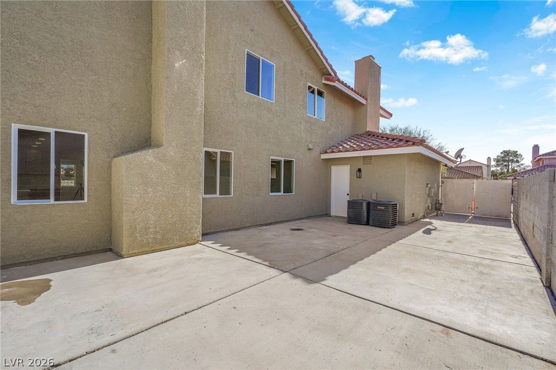 A spacious concrete patio spans the rear exterior of this two-story stucco residence.