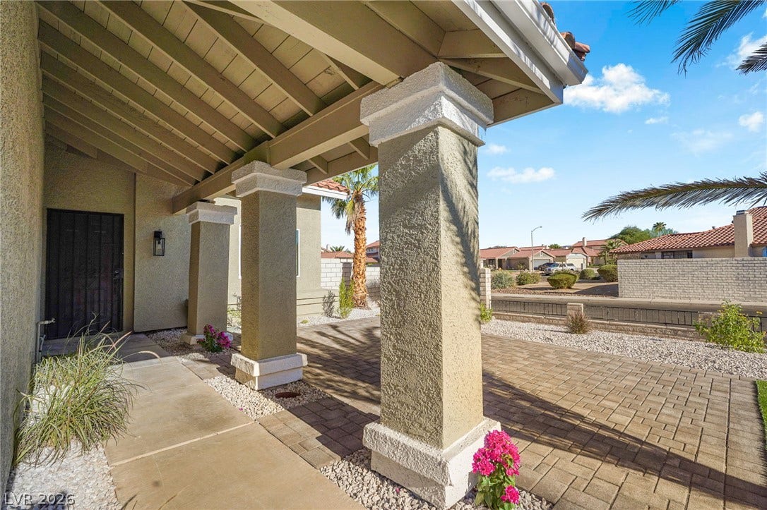 An inviting covered entryway features substantial stucco pillars and timeless paver detailing.