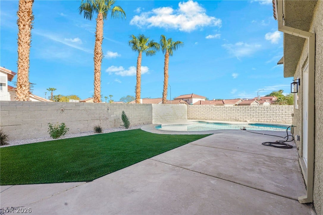 An inviting backyard oasis features a concrete patio, green turf, and a private pool.