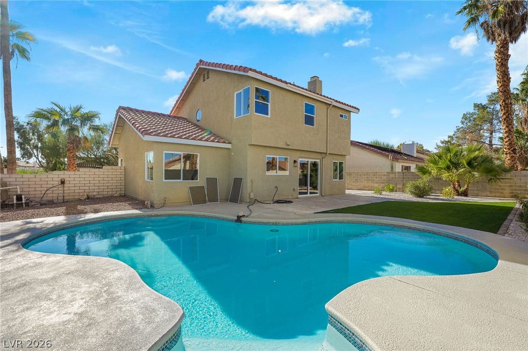 An inviting backyard oasis features a shimmering in-ground pool alongside a classic stucco exterior.