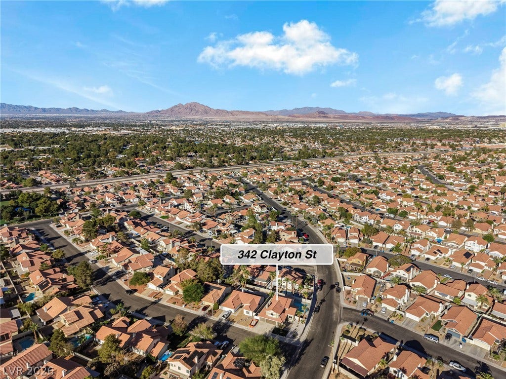 An aerial perspective showcases the surrounding neighborhood with distant mountain ranges under a blue sky.