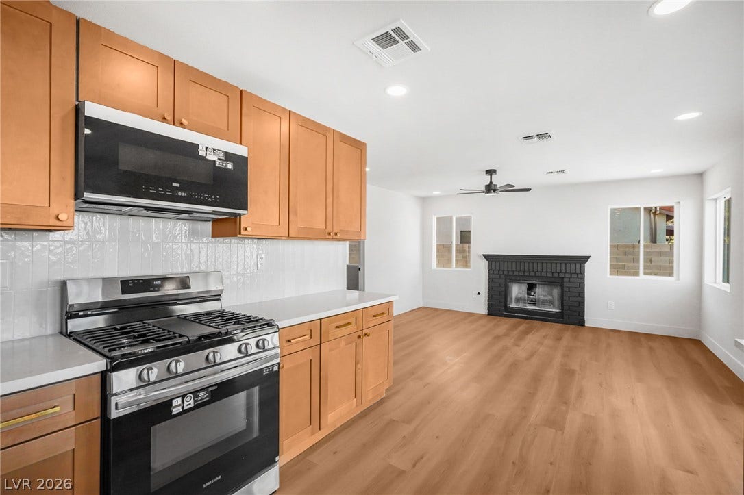 Warm wood cabinetry highlights a modern kitchen opening directly to a fireplace-centered living area.