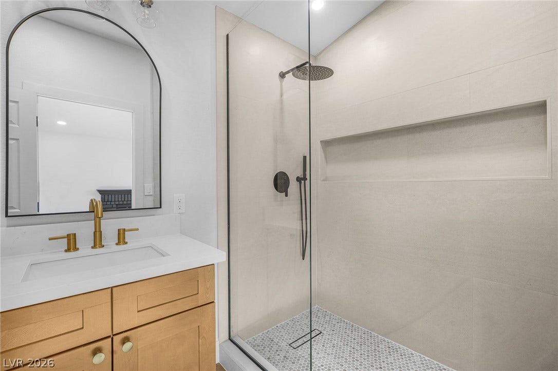 Modern stone tile lines a spacious walk-in shower adjacent to a sleek single vanity.