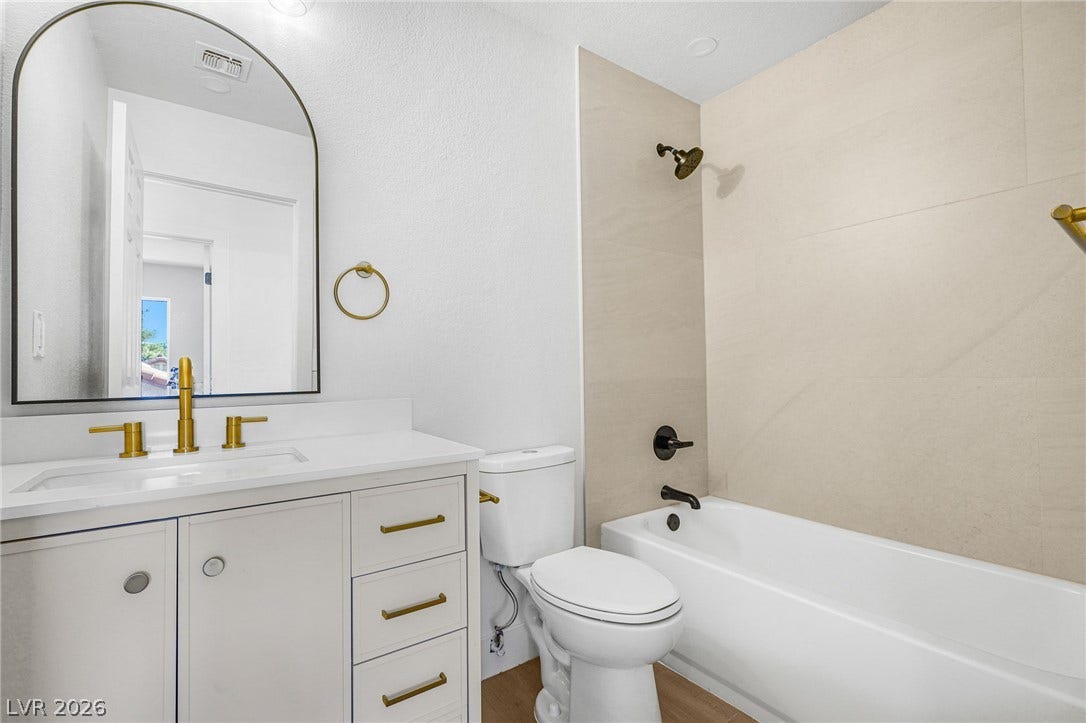 Elegant gold hardware pairs beautifully with the modern vanity and tiled alcove tub.