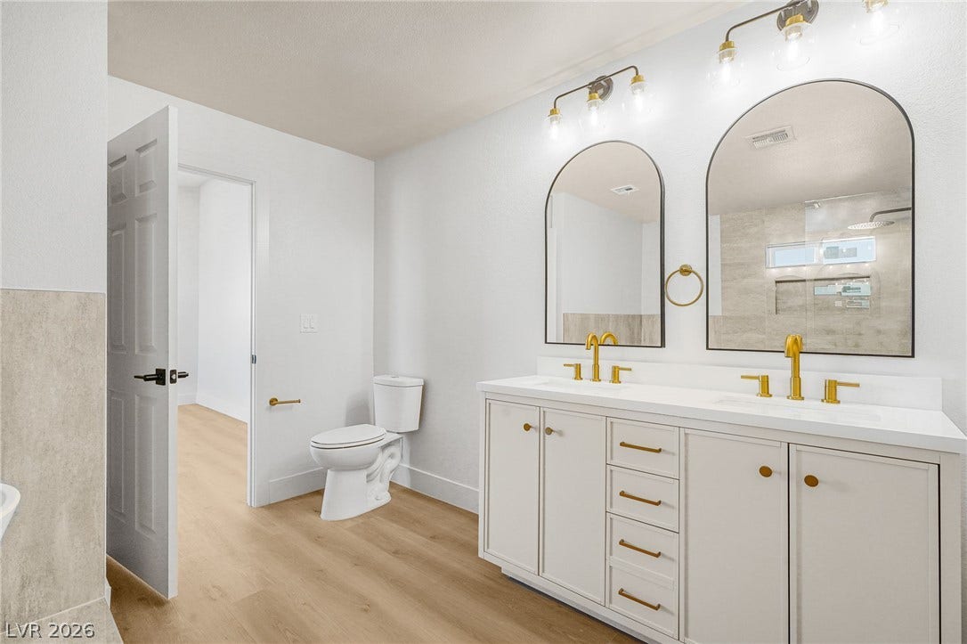 Double vanities with gold-toned fixtures complement the wood-look flooring in this renovated bathroom.
