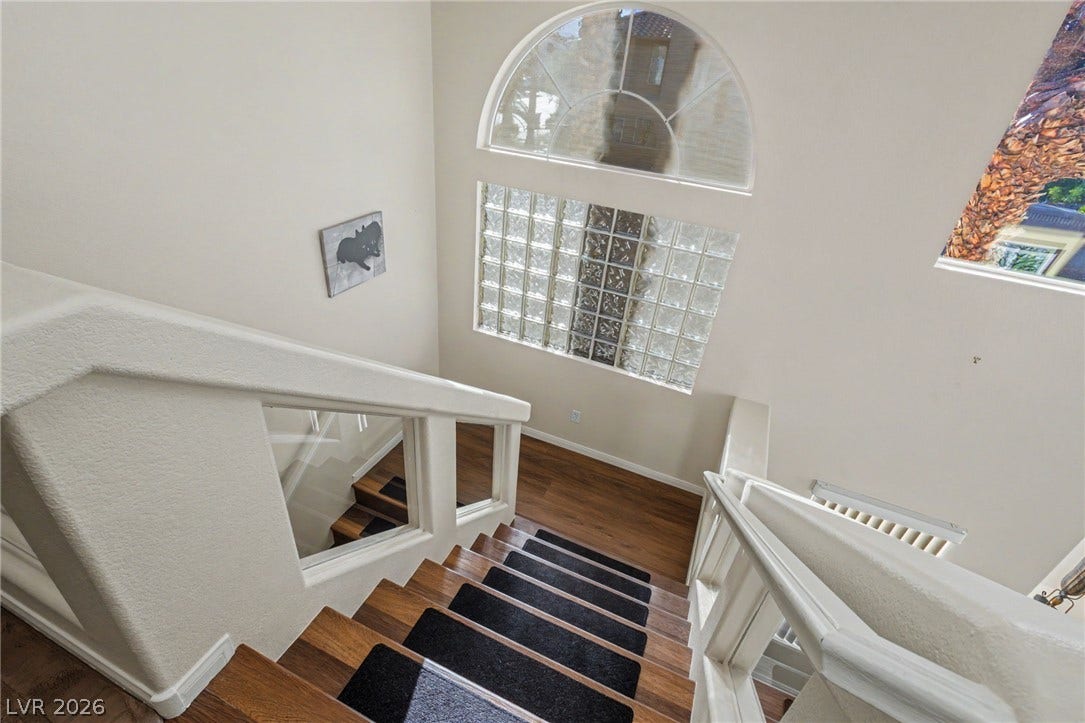 A spacious multi-level staircase is illuminated by architectural glass blocks and a large arched window.