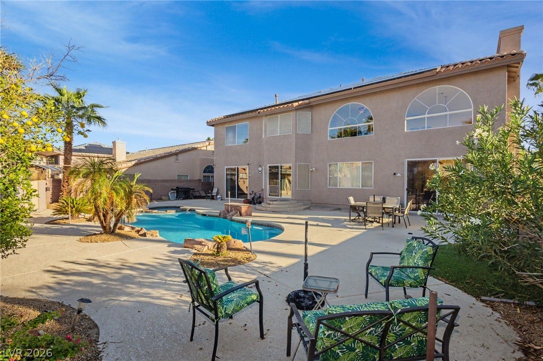 A sparkling in-ground pool anchors this sprawling paved backyard beneath a clear desert sky.