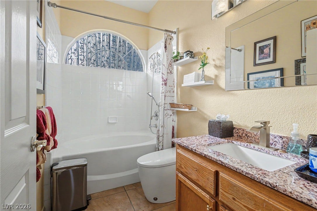 A spacious soaking tub is illuminated by a decorative arched window in this well-appointed bathroom.