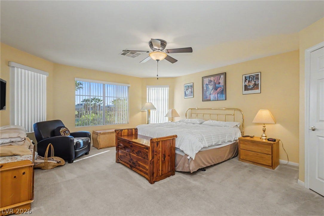 Sunlight streams through large windows into this comfortable bedroom with soft carpeting.