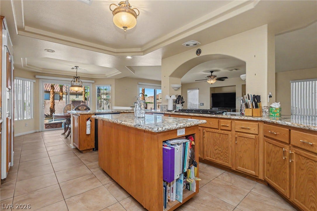 An open kitchen layout features rich wood cabinetry, granite countertops, and tiled floors.