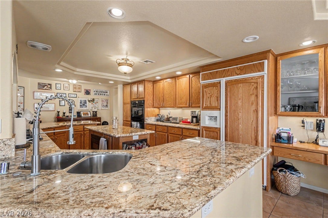 Polished granite countertops complement warm wood cabinetry and detailed recessed ceiling architectural features.