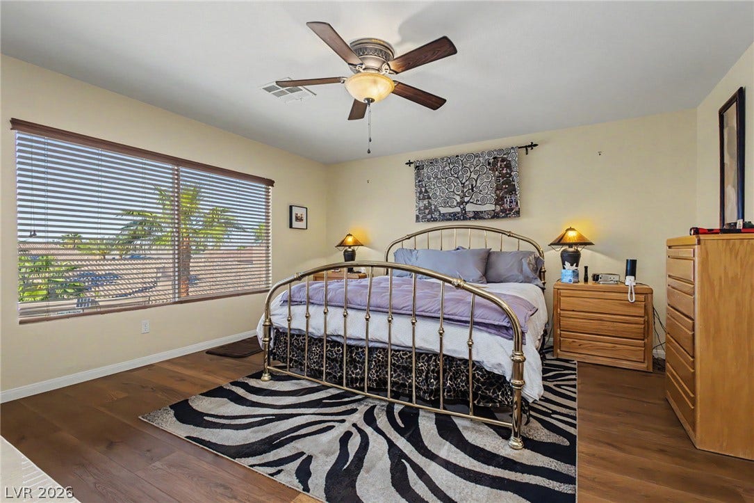Gleaming wood floors anchor this comfortable bedroom, complete with a wide window framing outdoor palms.