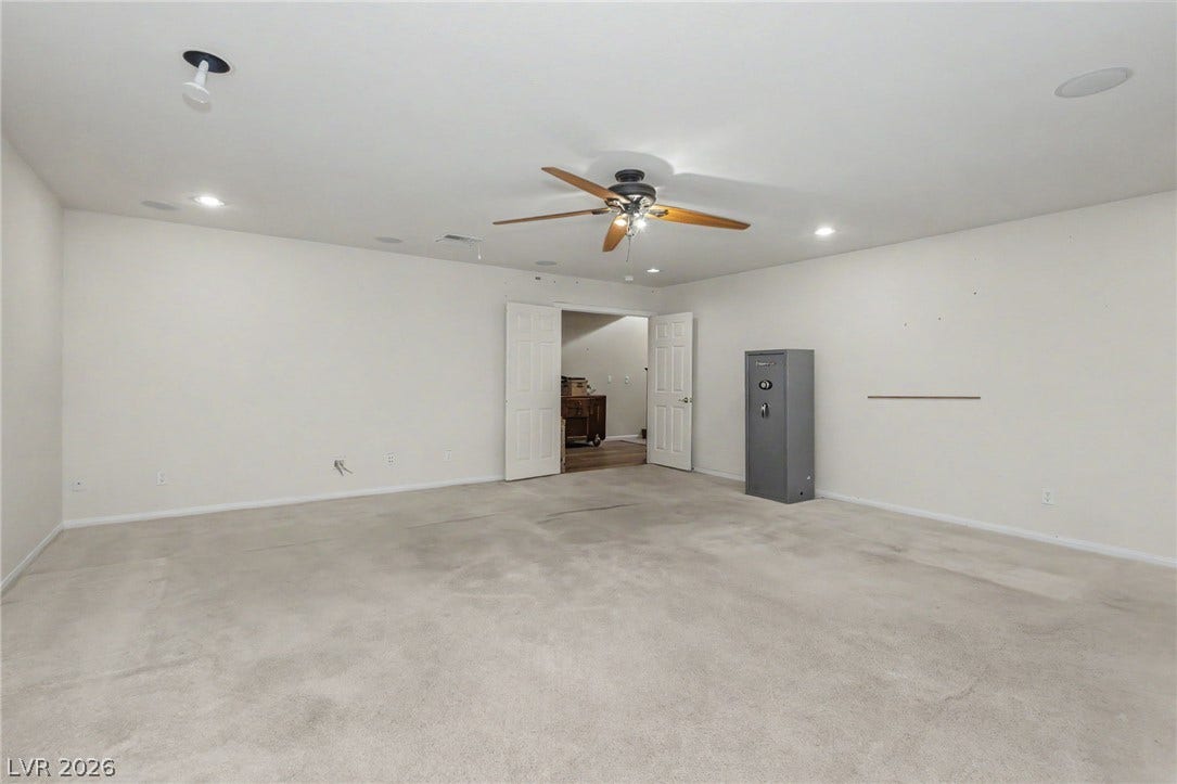 Double doors open to a spacious basement room featuring soft neutral carpeting and recessed lighting.