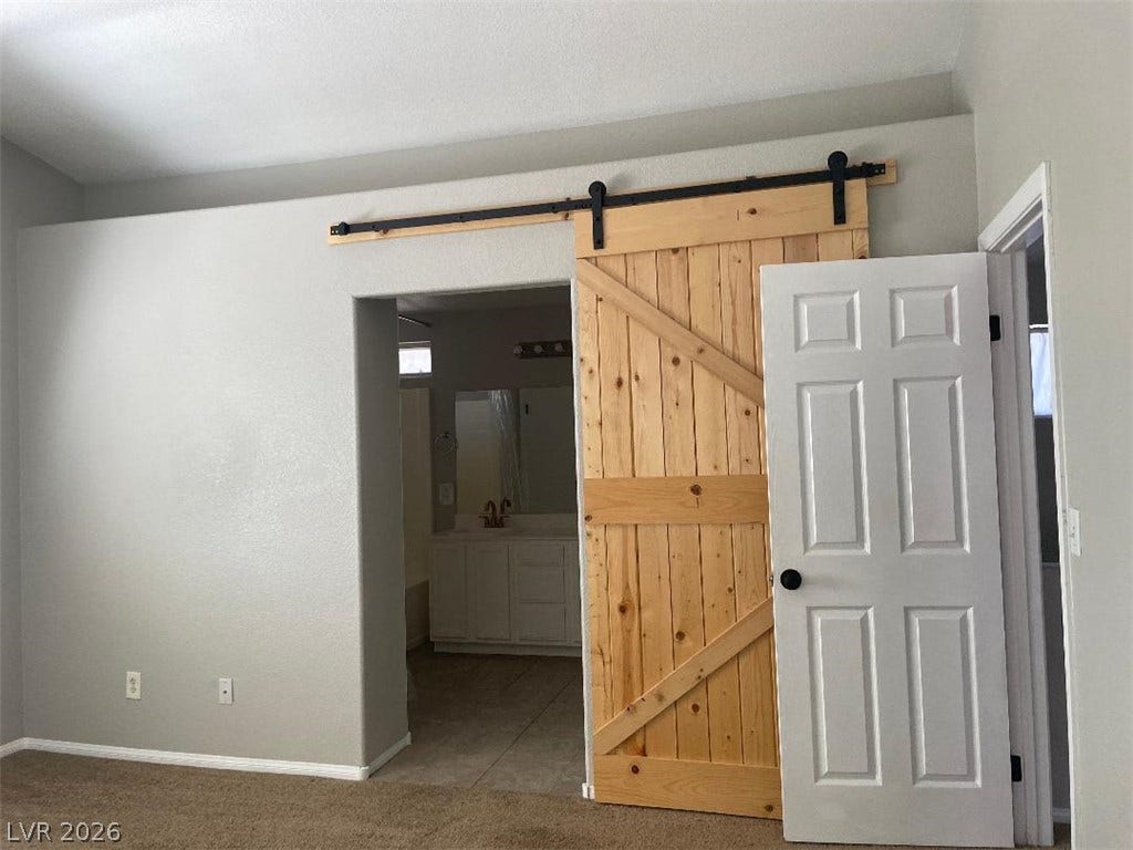 3025 Sunrise Bay Avenue, North Las Vegas, NV 89031 Plush carpeting and a rustic sliding barn door enhance this comfortable bedroom suite.