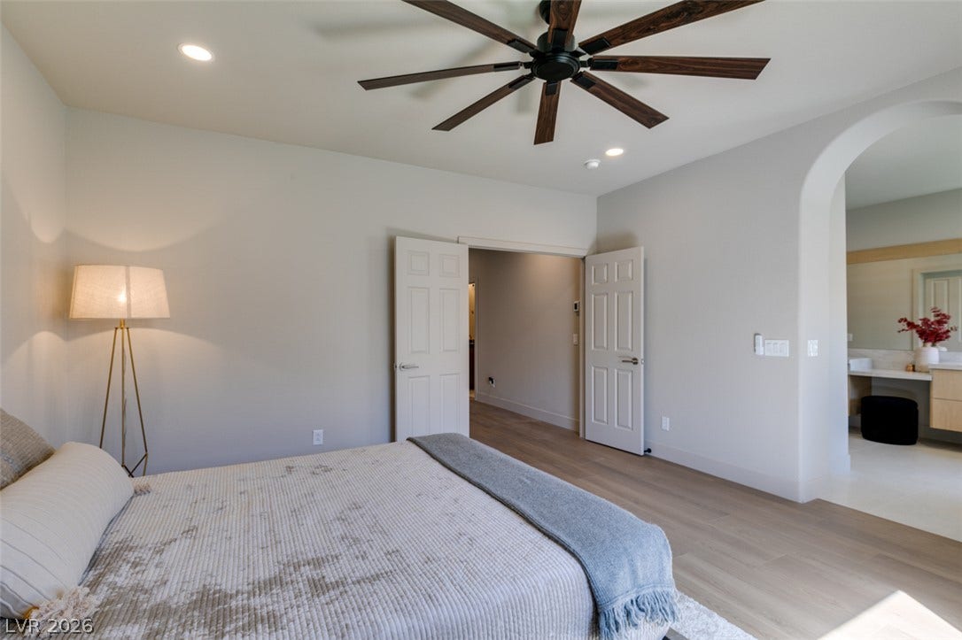 2897 Sunlit Glade Avenue, Henderson, NV 89074 An arched doorway leads to the master bathroom from this bedroom with wood flooring.