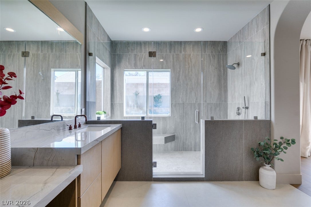 2897 Sunlit Glade Avenue, Henderson, NV 89074 A spacious walk-in shower lined with stone tile defines this modern primary bathroom.