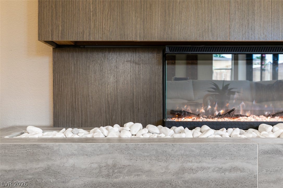 2897 Sunlit Glade Avenue, Henderson, NV 89074 A modern gas fireplace is set within a sleek stone hearth and textured wood paneling.