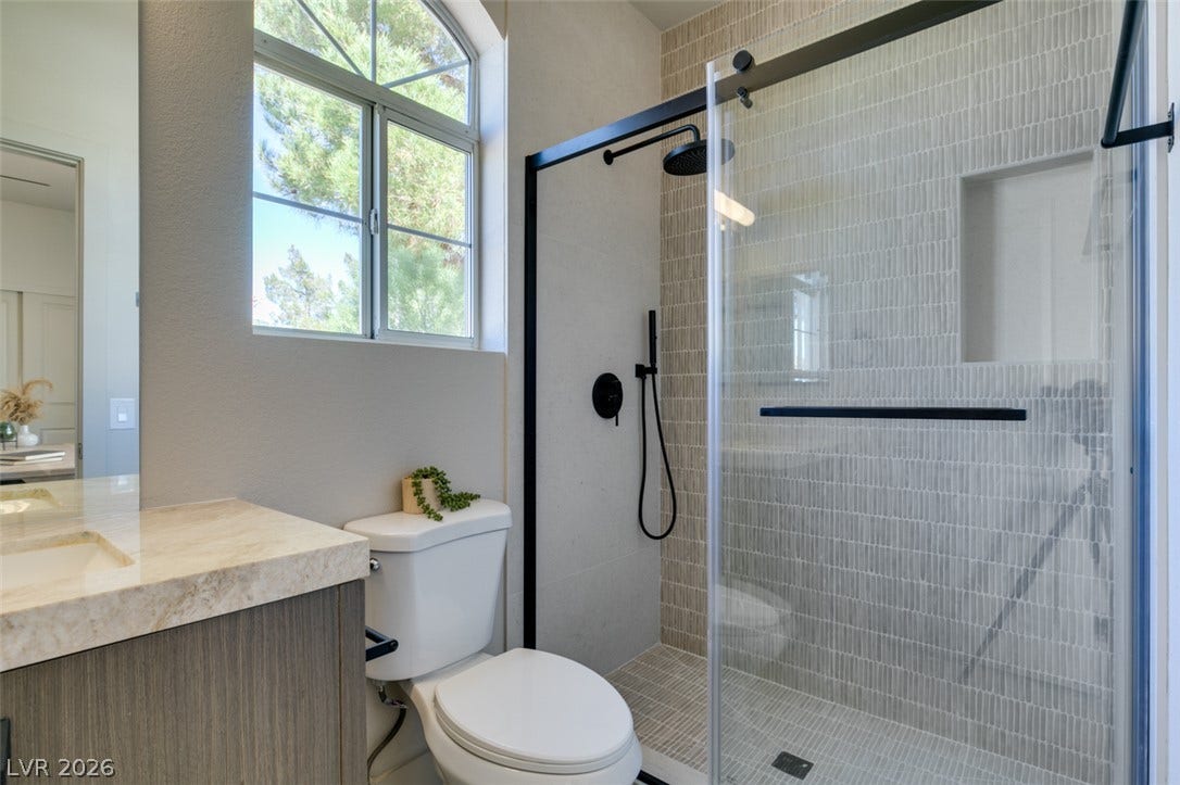 2897 Sunlit Glade Avenue, Henderson, NV 89074 An arched window floods the neutral-toned bathroom and tiled walk-in shower with natural light.