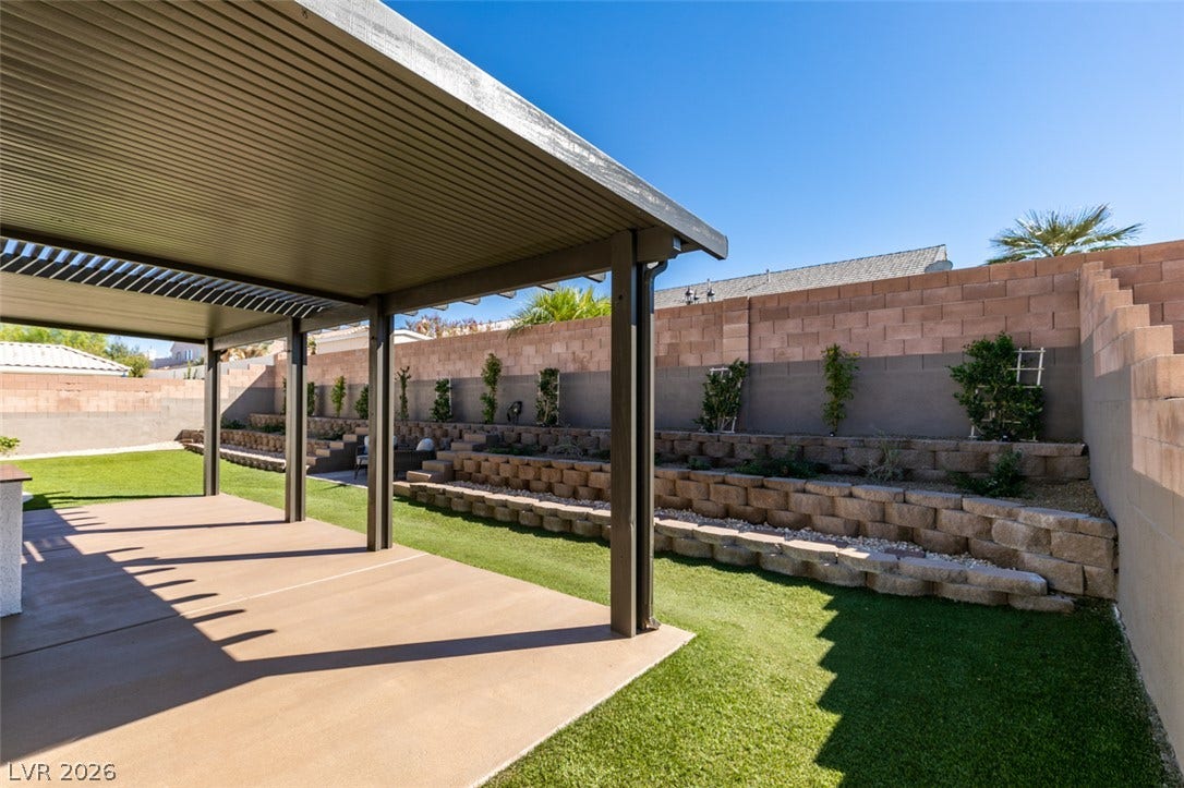 2897 Sunlit Glade Avenue, Henderson, NV 89074 An inviting covered patio overlooks a beautifully landscaped, tiered backyard with synthetic turf.