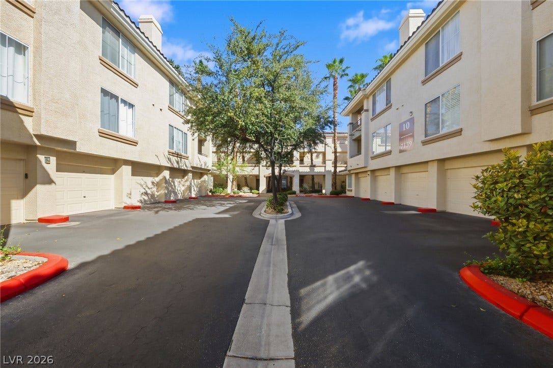 7139 S Durango Drive, #110, Las Vegas, NV 89113 Multi-story stucco buildings flank a paved driveway with integrated garage parking.